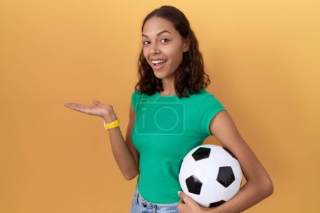Téléchargez les photos : Jeune femme hispanique tenant ballon pointant de côté avec les mains ouvertes paumes montrant l'espace de copie, présentant la publicité souriant heureux excité - en image libre de droit