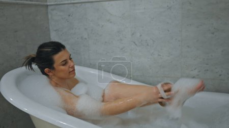 Téléchargez les photos : Une jeune femme détendue profite d'un bain moussant dans un cadre de salle de bain propre et moderne. - en image libre de droit
