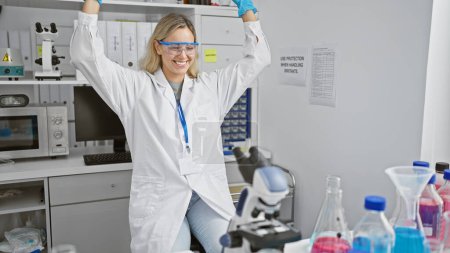 Téléchargez les photos : Une jeune femme scientifique joyeuse célèbre dans un cadre de laboratoire, entourée d'équipements et de produits chimiques, soulignant l'innovation et le succès. - en image libre de droit