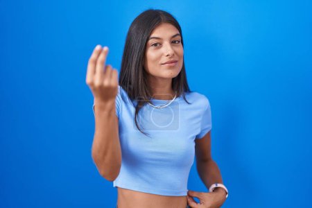 Foto de Morena joven mujer de pie sobre fondo azul haciendo gesto italiano con la mano y los dedos expresión de confianza - Imagen libre de derechos