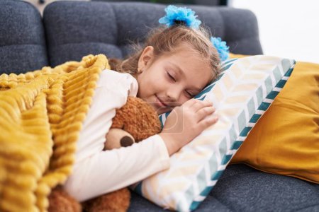 Adorable chica caucásica abrazando oso de peluche durmiendo en el sofá en casa