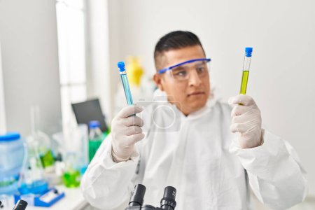 Téléchargez les photos : Jeune homme latino-scientifique portant des tubes à essai uniformes de protection contre les covidés en laboratoire - en image libre de droit