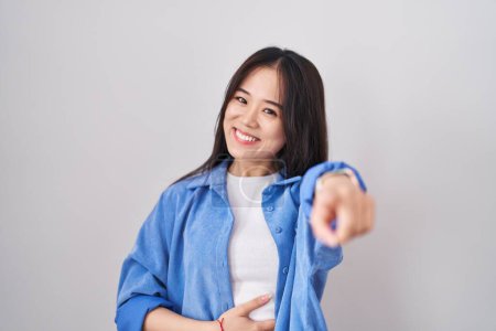 Foto de Joven mujer china de pie sobre fondo blanco riéndose de ti, señalando con el dedo a la cámara con la mano sobre el cuerpo, expresión de vergüenza - Imagen libre de derechos