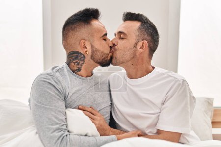 Foto de Dos hombres pareja sentada en la cama abrazándose besándose en el dormitorio - Imagen libre de derechos
