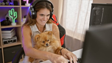 Foto de Joven mujer hispana, una radiante streamer amante de los perros, transmite con confianza el juego en la computadora mientras juega en la sala de juegos en casa iluminada por la noche - Imagen libre de derechos