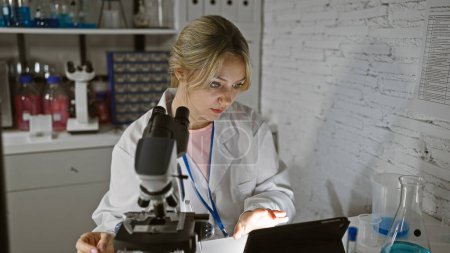 Eine junge kaukasische Wissenschaftlerin analysiert die Ergebnisse auf einer Tablette im Labor, umgeben von medizinischem Gerät.