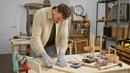 Junger Mann schleift Holz auf einer Werkbank in einer gut ausgestatteten Tischlerei
