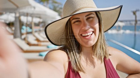 Téléchargez les photos : Femme souriante en chapeau de soleil jouissant d'une ambiance de luxe au bord de la piscine par une journée ensoleillée, incarnant détente et style de vie. - en image libre de droit