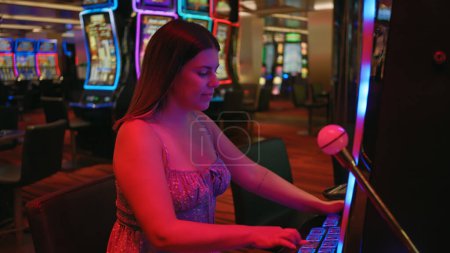 Photo for A young adult woman plays slot machines at a neon-lit casino, embodying leisure and nightlife entertainment. - Royalty Free Image
