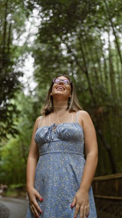 Téléchargez les photos : Belle femme hispanique avec des lunettes, souriant avec confiance alors qu'elle se tient parmi la forêt de bambous luxuriante de kyoto, regardant autour de elle, pleine de joie et d'étonnement. - en image libre de droit
