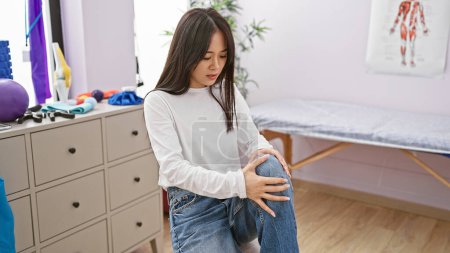 A young asian woman assesses her knee pain in a physical therapy clinic.