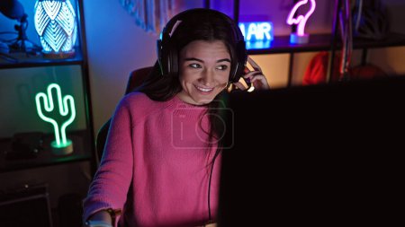 Foto de Una joven hispana disfruta jugando por la noche en una acogedora sala interior con vibrantes luces de neón. - Imagen libre de derechos