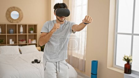 Photo for Handsome hispanic man with beard wearing virtual reality headset in modern bedroom - Royalty Free Image