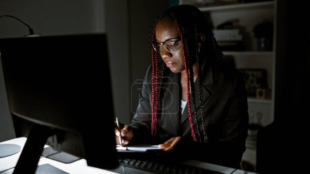 Téléchargez les photos : Travaillant la magie nocturne, une femme d'affaires afro-américaine la balance au bureau, prend des notes et jongle avec un appel vidéo. dépeignant le succès elle commande la salle intérieure avec confiance - en image libre de droit