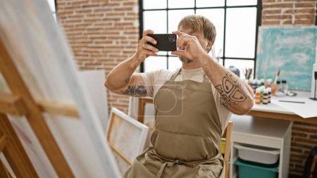 Homme blond avec des tatouages prenant des photos dans un studio d'art