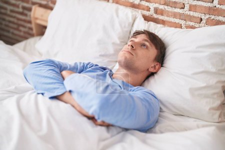 Téléchargez les photos : Jeune homme caucasien stressé couché sur le lit dans la chambre - en image libre de droit