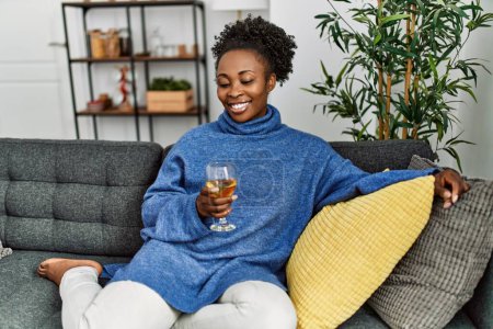 Photo for African american woman drinking glass of wine sitting on table at home - Royalty Free Image