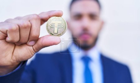 Joven trabajador de negocios latino sosteniendo moneda cripto atadura sobre fondo blanco aislado