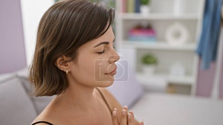 Photo for Heartfelt prayers from young, beautiful hispanic woman, with eyes closed and relaxing on a sofa at home, meditating to find inner balance - Royalty Free Image