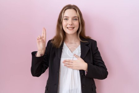 Foto de Mujer de negocios caucásica joven con chaqueta negra sonriendo jurando con la mano en el pecho y los dedos hacia arriba, haciendo un juramento de lealtad promesa - Imagen libre de derechos