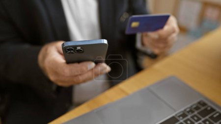 Téléchargez les photos : Les mains d'un cadre supérieur engagées dans des achats en ligne avec carte de crédit sur smartphone au bureau - en image libre de droit