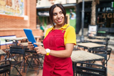 Téléchargez les photos : Jeune belle serveuse arabe souriante confiante en utilisant le pavé tactile à la terrasse du café - en image libre de droit
