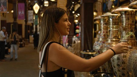 Young adult woman browses traditional wares at a souk in dubai, exemplifying tourism and culture.