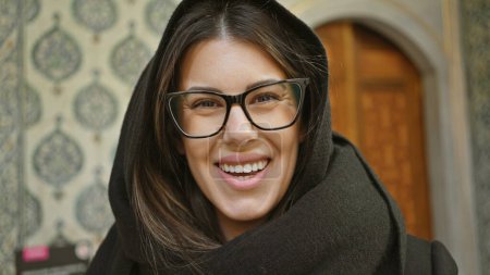 Photo for A smiling young woman with glasses in a black coat poses inside the historical topkapi palace in istanbul, representing tourism and culture. - Royalty Free Image