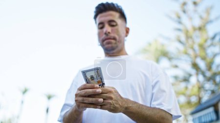Young hispanic man counting dollars at street