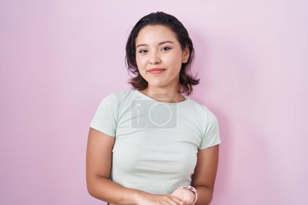 Téléchargez les photos : Jeune femme hispanique debout sur fond rose avec les mains jointes et les doigts croisés souriant détendu et joyeux. succès et optimisme - en image libre de droit