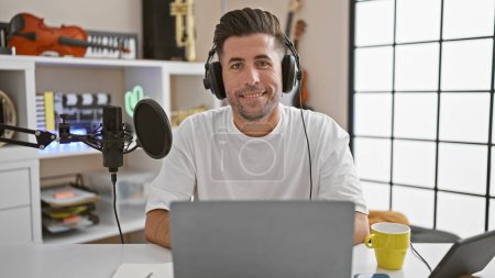 Foto de Joven reportero de radio hispano con auriculares sonriendo en estudio de radio - Imagen libre de derechos