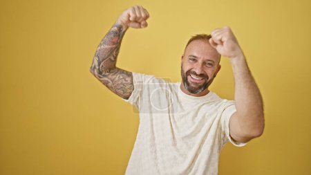 Photo for Cheerful young man confidently celebrates his win, arms raised in joy, standing against an isolated yellow background, radiating happiness - Royalty Free Image