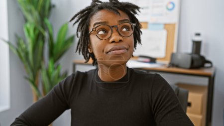 Foto de Retrato de una joven contemplativa negra con rastas con gafas en su oficina - Imagen libre de derechos