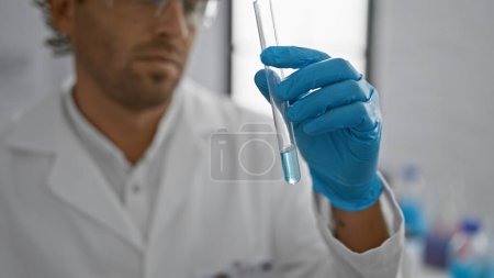 Téléchargez les photos : Un homme hispanique barbu examine une éprouvette dans un laboratoire intérieur, représentant la science et les soins de santé. - en image libre de droit