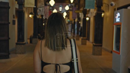 Téléchargez les photos : Une jeune femme explore un souk arabe traditionnel à Dubai avec des lanternes et une architecture locale. - en image libre de droit