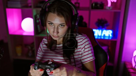 Téléchargez les photos : Jeune femme concentrée jouant à un jeu vidéo dans une salle de jeux colorée et éclairée au néon la nuit - en image libre de droit