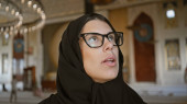 A young adult hispanic woman wearing a hijab and glasses looks upwards inside a doha mosque exhibiting islamic architecture. Stickers #703166092