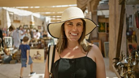 Téléchargez les photos : Une jeune femme souriante dans un chapeau de soleil explore un souk traditionnel animé de dubai débordant d'attrait touristique. - en image libre de droit