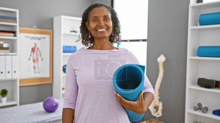 Photo for African american woman holding yoga mat in rehabilitation clinic interior - Royalty Free Image