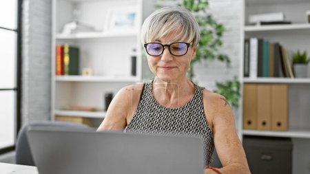 Mature hispanic woman with grey hair working confidently in a modern office.
