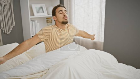 Téléchargez les photos : Jeune homme hispanique s'étirant dans une chambre moderne confortable au réveil. - en image libre de droit