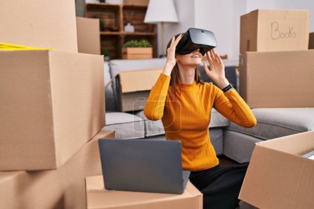 Téléchargez les photos : Jeune femme caucasienne jouer à un jeu vidéo en utilisant des lunettes de réalité virtuelle à la nouvelle maison - en image libre de droit
