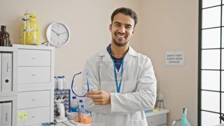 Téléchargez les photos : Beau jeune homme en blouse de laboratoire souriant à l'intérieur dans un laboratoire moderne - en image libre de droit