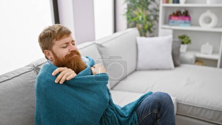 Le conte froid de l'hiver, beau jeune rouquin gelant, trouve le confort douillet dans une couverture chaude, assis sur le canapé, luttant contre le froid à l'intérieur à la maison.