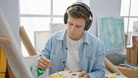 Foto de Joven artista caucásico dibujando enfocado a escuchar música en estudio de arte - Imagen libre de derechos