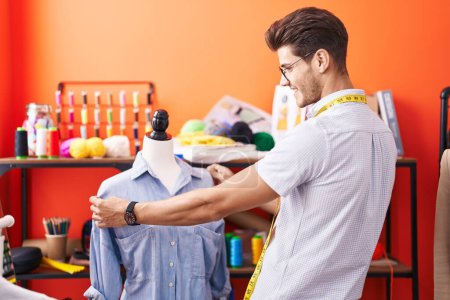 Téléchargez les photos : Young hispanic man tailor smiling confident measuring shirt at atelier - en image libre de droit