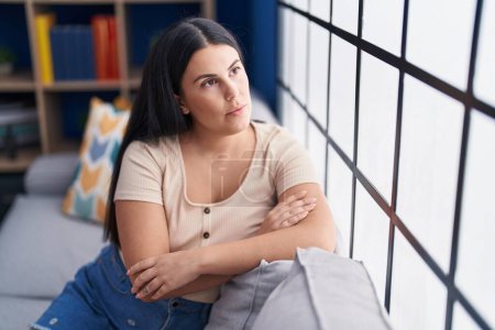 Photo for Young beautiful hispanic woman sitting on sofa with serious expression at home - Royalty Free Image