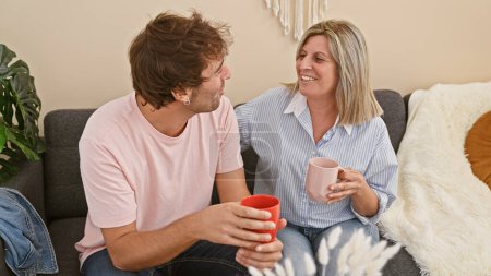 Photo for Joyful mother and son sitting together on a sofa at home, enjoying a cup of coffee while having a lovely chat in their cozy living room - Royalty Free Image