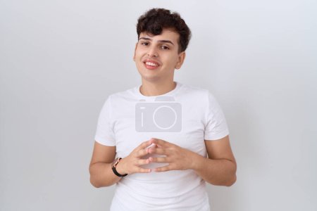 Téléchargez les photos : Jeune homme non binaire portant casual t-shirt blanc mains ensemble et doigts croisés souriant détendu et joyeux. succès et optimisme - en image libre de droit