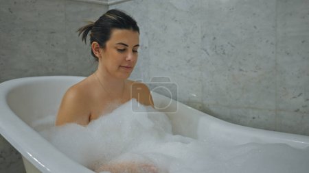 Photo for A young woman enjoys a relaxing bath in a home bathroom, surrounded by bubbles and serenity. - Royalty Free Image